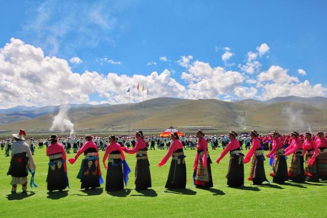 The dressed-up Tibetans are dancing on the grassland.